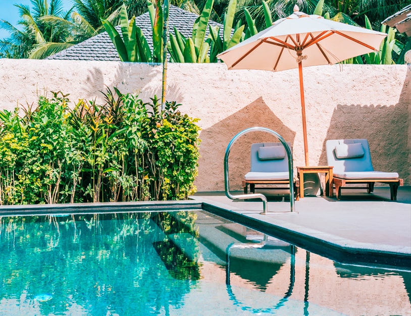 Ambiente com piscina e um guarda sol com duas cadeiras