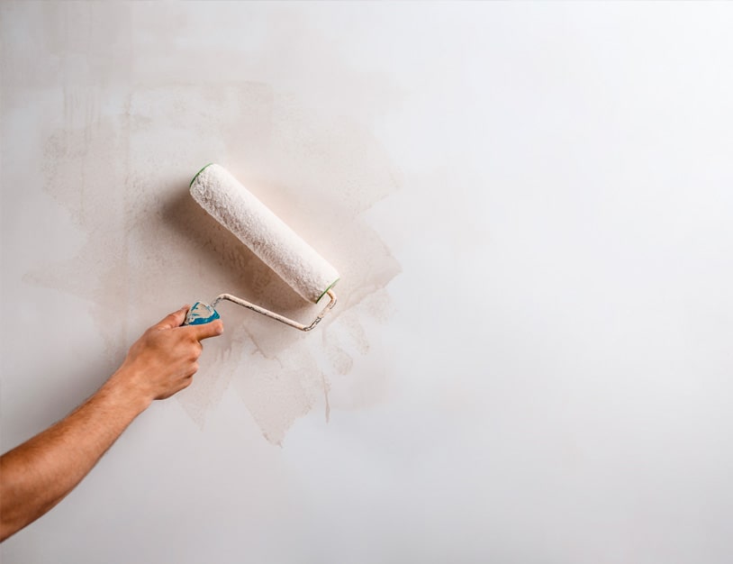 Uma mão segurando um rodo e passando na parede para pintura